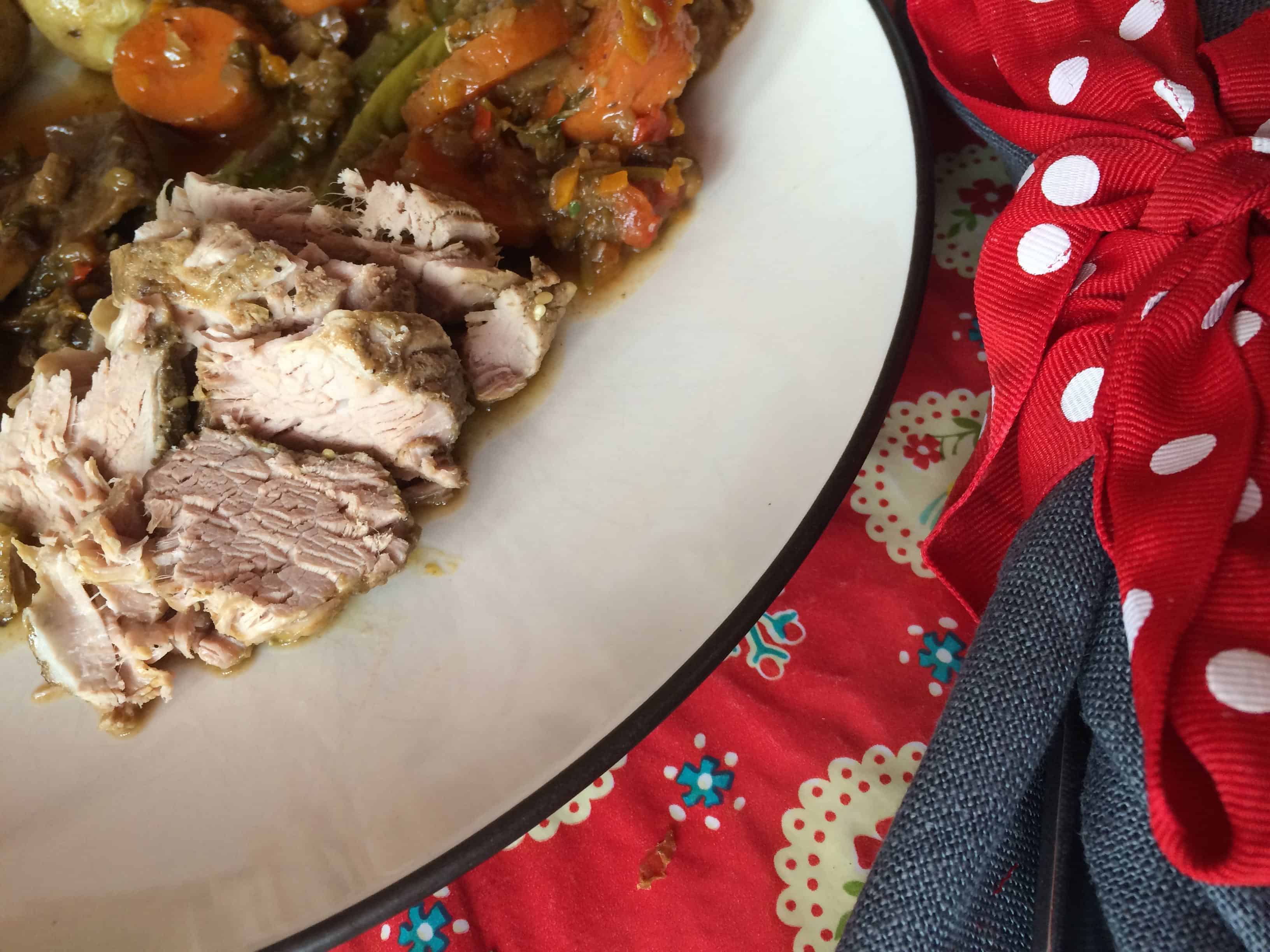 Sliced Instant Pot Zaatar Pork with Vegetables served on an off white stoneware plate. Dark grey fabric napkin on the right with spotty ribbon (red background with white polka dots) on a red patterned tablecloth