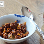 Feisty Tapas Quick Instant Pot Lime Pickle served on a small bowl on a brown wooden floorboard background with a silver spoon to the right. Part of the lime pickle jar can be seen on the right of the photo. Feisty Tapas logo is shown on the top left of the photo