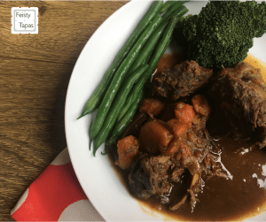 Delicious Feisty Tapas Instant Pot Pressure Cooker Ox Cheeks in Stout served with lots of sauce and green beans in a deep white plate with a wooden background and red and white polka dot fabric
