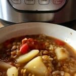 Instant Pot Spanish Lentil Soup (Lentejas) by Feisty Tapas served on a deep white dish with an Instant Pot DUO in the background. Green lentils, chorizo, potatoes... but it's super easy to make it a vegetarian or vegan lentil soup. Lentejas is a traditional Spanish Lentil Soup. An authentic Spanish dish