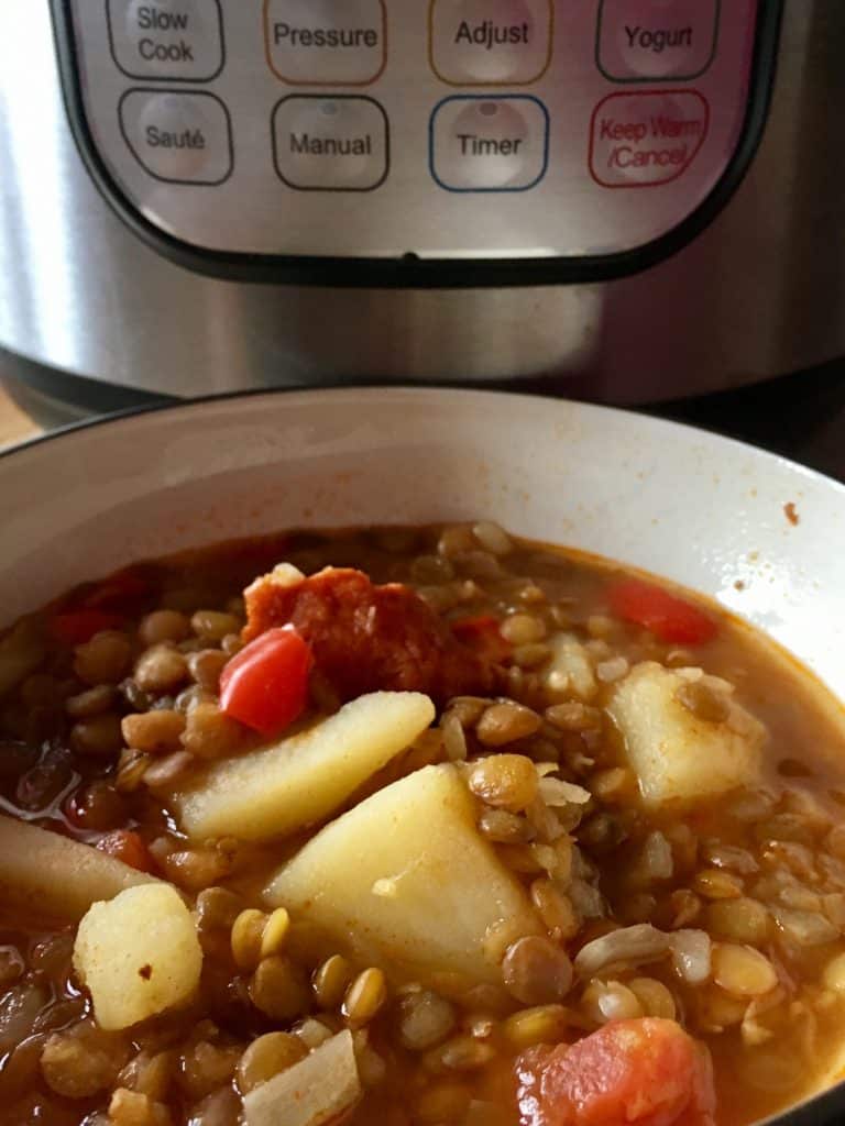 Instant Pot Spanish Lentil Soup (Lentejas) by Feisty Tapas served on a deep white dish with an Instant Pot DUO in the background. Green lentils, chorizo, potatoes... but it's super easy to make it a vegetarian or vegan lentil soup. Lentejas is a traditional Spanish Lentil Soup. An authentic Spanish dish