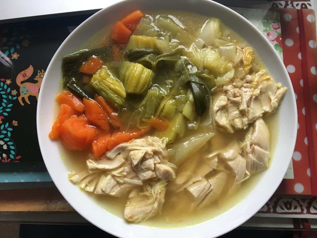 Delicious Feisty Tapas Instant Pot Chicken, Leek and Carrot soup ready to eat on a deep plate after chopping with sea salt to make it extra tasty. A super easy chunky soup served on a white deep plate. The photo shows a red and white polka dot notebook on the right