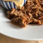 Instant Pot Pulled Pork with Creamy Paprika Sauce by Feisty Tapas. The pulled pork is served in a large white round serving dish and the sauce is looking delicious oozing from the side of a smaller blue and white striped bowl. On a wooden table