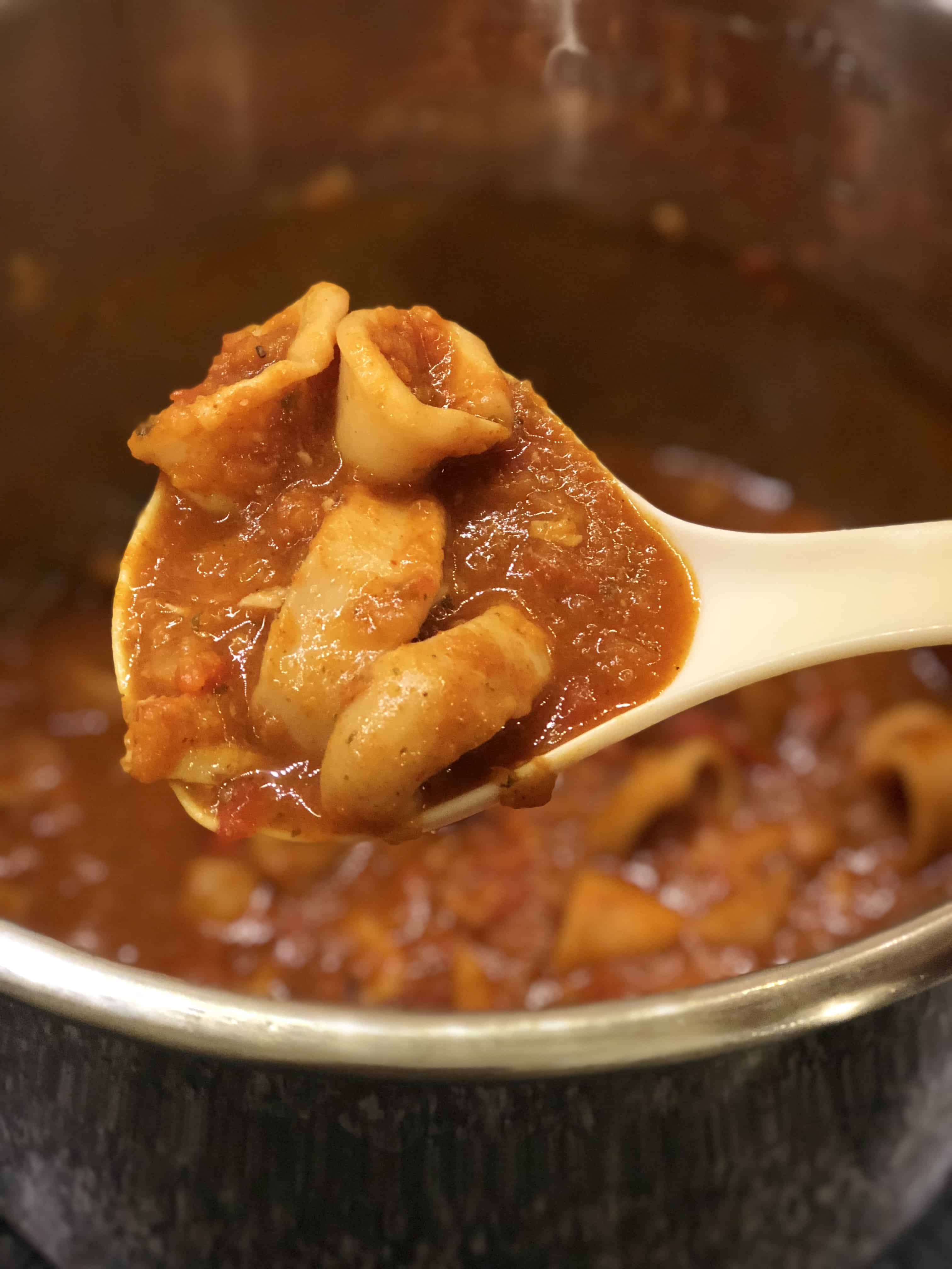 Instant Pot Squid Stew recipe by Feisty Tapas. Squid is really tender when pressure cooked and the sauce in this stew is delicious, with Spanish paprika hints. White ladle holding some of the stew with the Instant Pot's inner pot full of delicious Squid Stew in the background