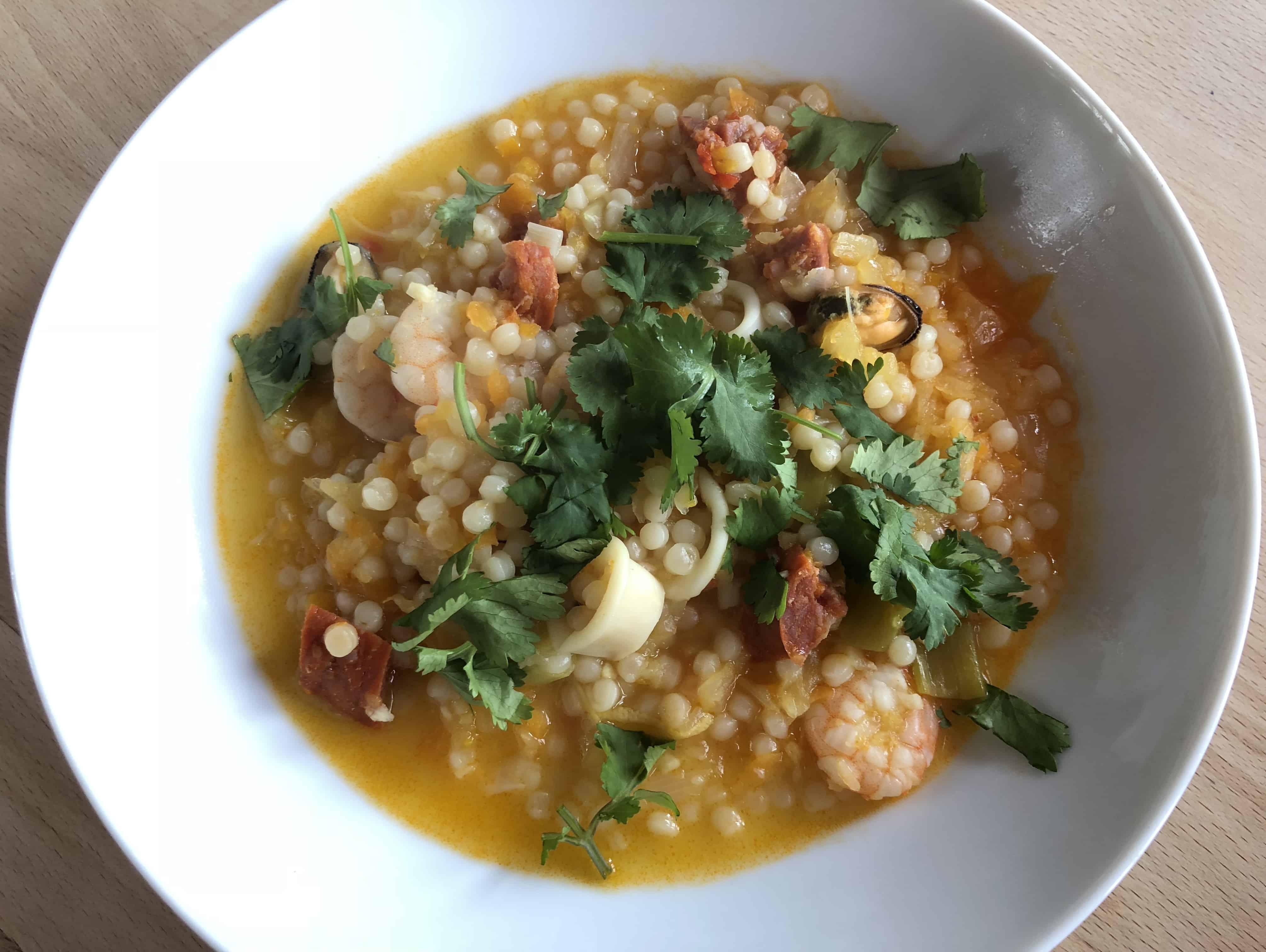 Delicious and super quick Instant Pot Giant Cous Cous with seafood served in a deep white dish against a light wooden table