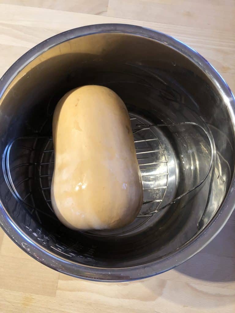 Whole butternut squash on the trivet of the Instant Pot ready to pressure cook to make peeling easier