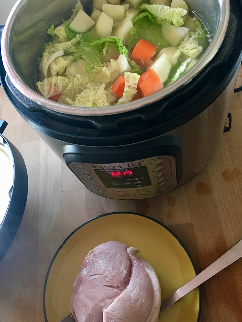 Pressure cooked gammon joint seen from above on a yellow plate. The cabbage, carrots and potatoes for the soup have been added to the stock and can be seen in the cooker from a above too