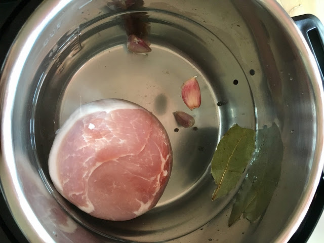 Photo from above of the water, gammon joint, garlic cloves and bay leaf inside the stainless steel inner pot of the Instant Pot Duo