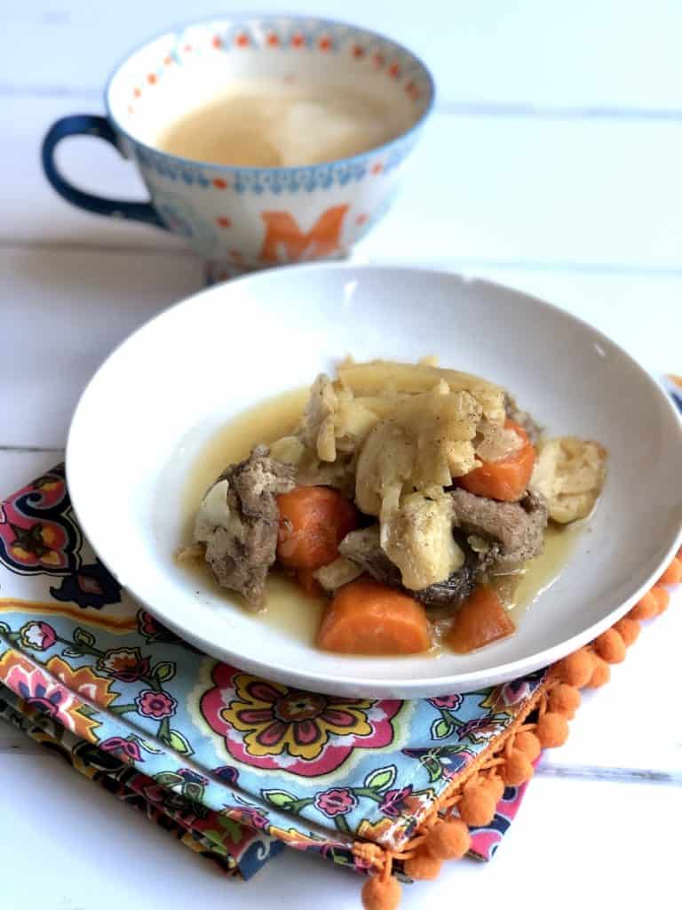 Instant Pot Pork and Cabbage recipe by Feisty Tapas - served on a white plate with a tea towel with orange pom poms and a mug with the initial M in the background and white worktop surface