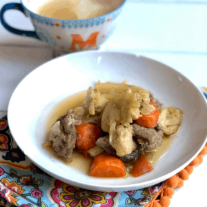 Instant Pot Pork and Cabbage recipe by Feisty Tapas - served on a white plate with a tea towel with orange pom poms and a mug with the initial M in the background - featured image