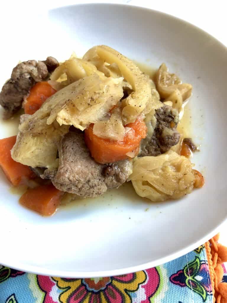 Instant Pot Pork and Cabbage recipe by Feisty Tapas - served on a white plate with a tea towel with orange pom poms