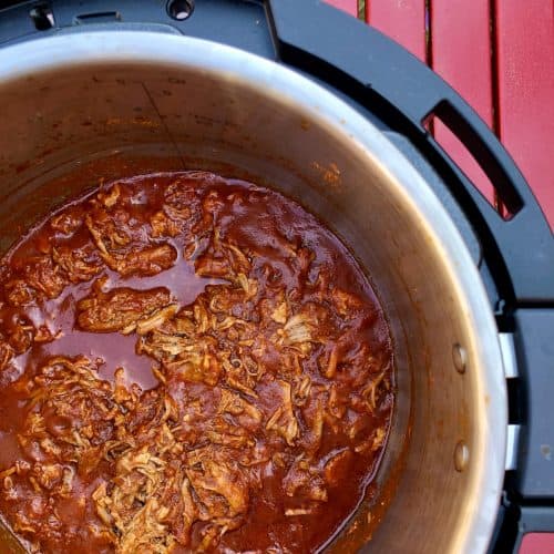 Photo of Cooked Easy Instant Pot BBQ Pulled Pork recipe by Feisty Tapas, seen from above inside the Instant Pot Duo Evo Plus against a red slatted surface