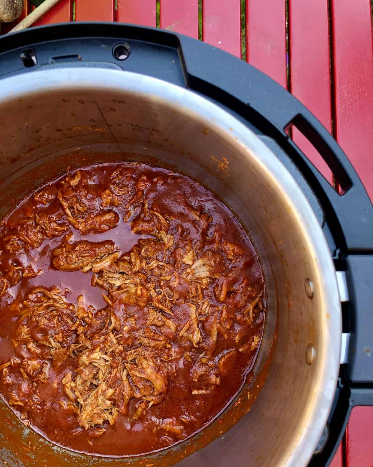 Photo of Cooked Easy Instant Pot BBQ Pulled Pork recipe by Feisty Tapas, seen from above inside the Instant Pot Duo Evo Plus against a red slatted surface