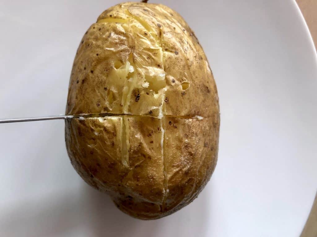 Instant Pot duo crisp baked potato view from above with potato still on trivet and other potato served with butter and cheese