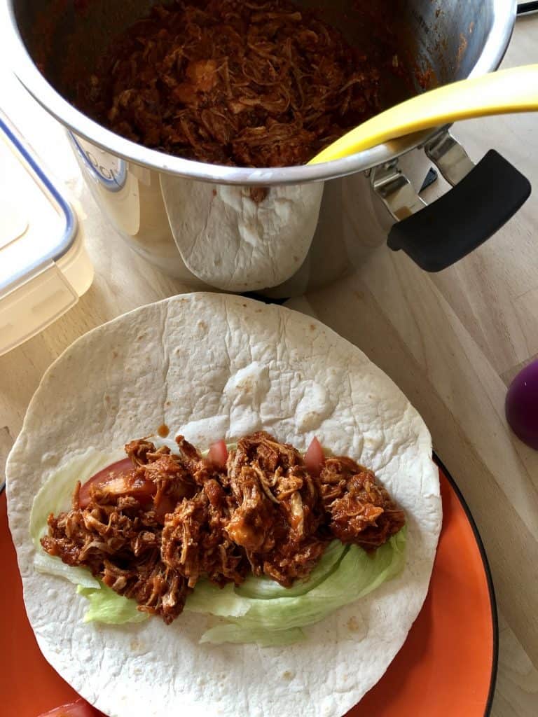 Delicious pulled pork served on a tortilla wrap with lettuce and tomatoes, on an orange plate, for an easy dinner