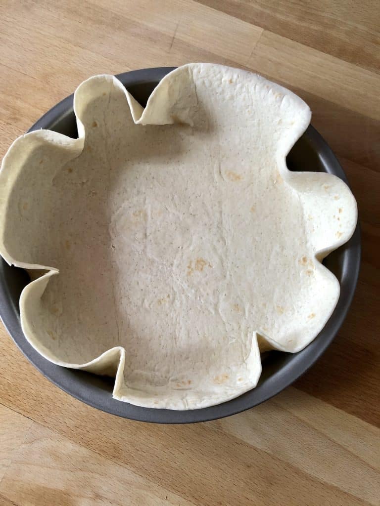 Tortilla wrap pressed into cake pan ready for toppings