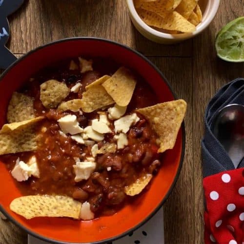 Mexican Bean soup served in an orange bowl with Doritos and cheese cubes