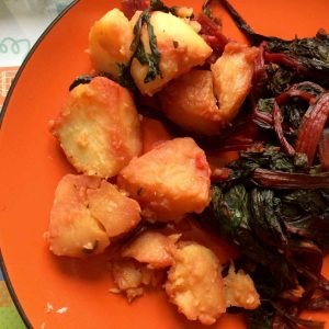 Thermomix Paprika Chard and Potatoes served on an orange plate, the potatoes to the left and the chard to the right