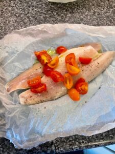 Fish parcel for Pressure Cooker Leek Risotto with Sea Bass. The raw fish sits on greaseproof paper with tomatoes scattered on top