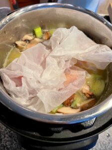 Fish parcel wrapped en papillote in greaseproof paper, placed above risotto ready to pressure cook Leek Risotto with Sea Bass