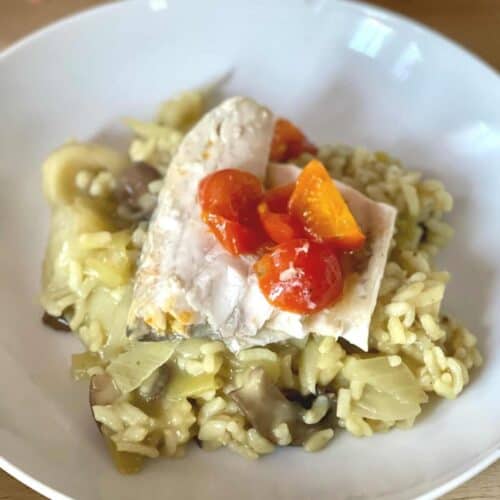 Pressure Cooker Leek Risotto with Sea Bass, the risotto is served with the white fish on top and the striking red of the tomatoes stands out on top