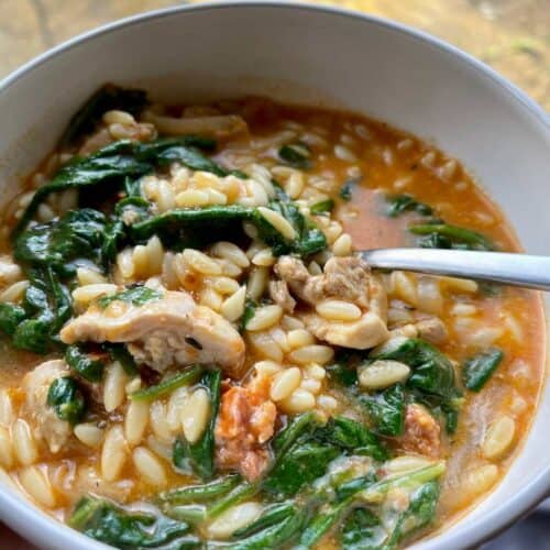 Pressure Cooker Chicken Chorizo Orzo with green leaves of spinach stirred through - seen from above on white bowl with grey rim