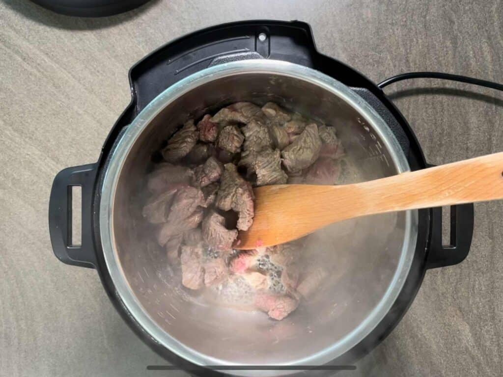 Diced beef seen from above while browning inside the stainless steel inner pot of the Instant Pot Duo