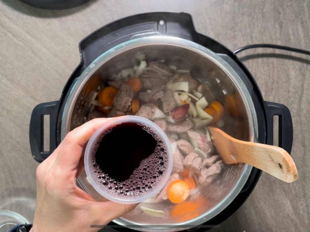 Red wine about to go into the beef stew seen from above inside the stainless steel inner pot of the Instant Pot Duo