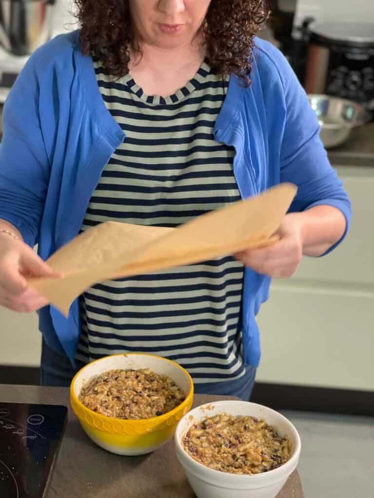 Catherine Phipps placing greaseproof paper with pleat on a pudding basin. On a table we can see two pudding basins with Christmas Pudding mix, one of the basins is yellow and the other one is white