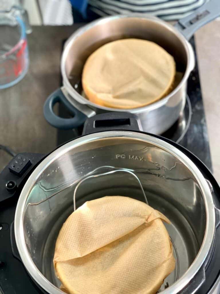 Pudding basins covered in greaseproof paper with a pleat ready to pressure cook inside an Instant Pot electric pressure cooker and a stove-top pressure cooker
