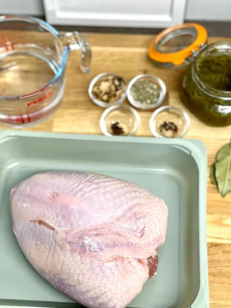 Ingredients for pressure cooking turkey crown laid out on a wooden chopping board, seen from above, turkey crown placed in a light green container