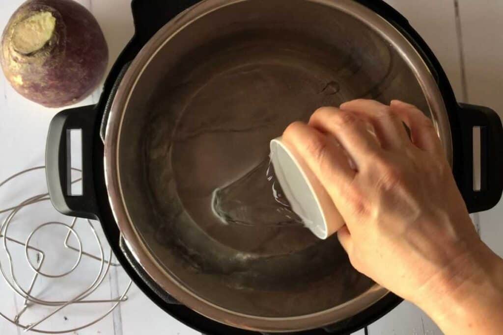 Adding water to the stainless steel inner pot of the Instant Pot Duo. The swede is on the top left of the picture and the trivet / steamer rack on the bottom left
