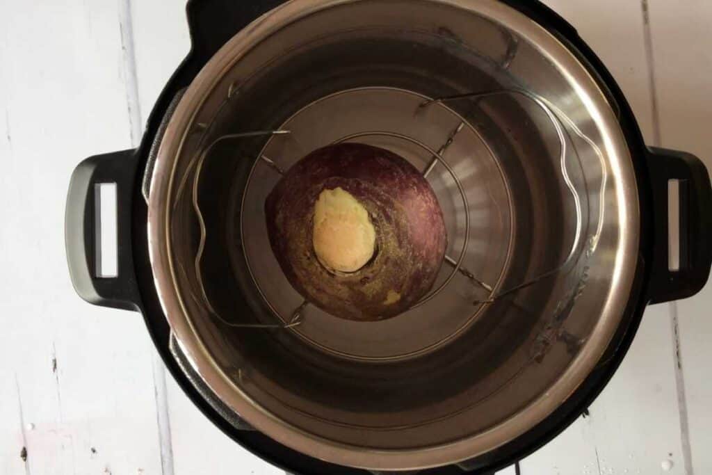 Whole uncooked swede seen from above resting on the trivet / steamer rack inside the stainless steel inner pot of the Instant Pot Duo, against a white background