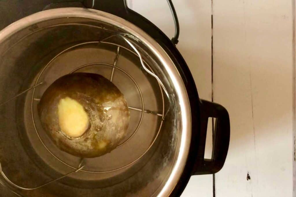 Whole swede right after pressure cooking, seen from above resting on the trivet / steamer rack inside the stainless steel inner pot of the Instant Pot Duo, against a white background