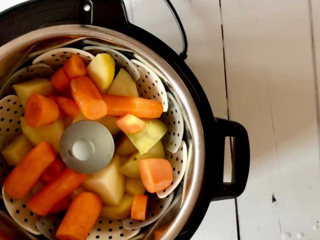 Carrot and swede seen in big chunks in a steamer basket, shot from above inside an Instant Pot