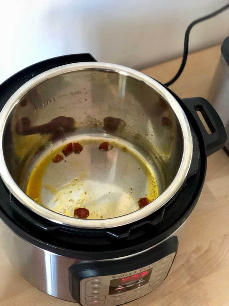 Instant Pot Duo Mini seen from above on a lightly coloured wooden surface, with the diced chorizo sausage sautéing inside