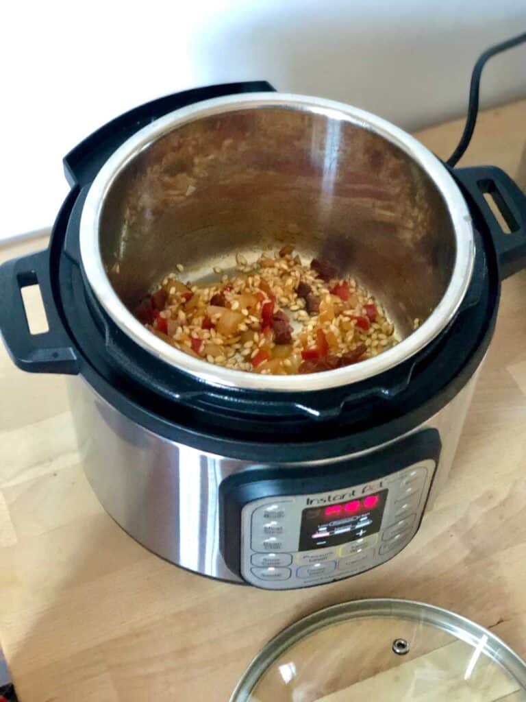 Toasting the arborio risotto rice before adding the stock and pressure cooking in the Instant Pot Duo Mini, on a light wooden surface with the glass lid on it