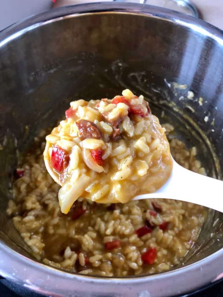 A scoop of Pressure Cooker Chorizo risotto being held above the rest of the pot full of risotto
