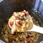 A ladleful of pressure cooker chorizo risotto seen from above, held above an Instant Pot stainless steel inner pot full of rice