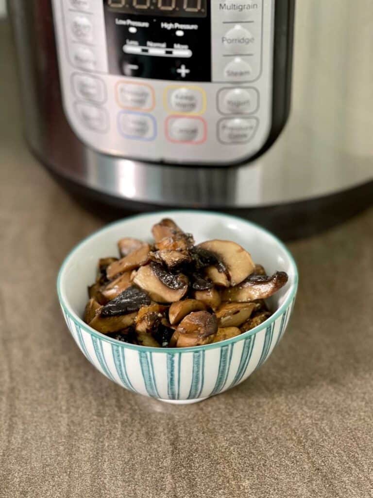 Garlic Mushrooms served in a white and green stripy bowl with an Instant Pot Duo electric pressure cooker in the background, on a brown kitchen counter surface