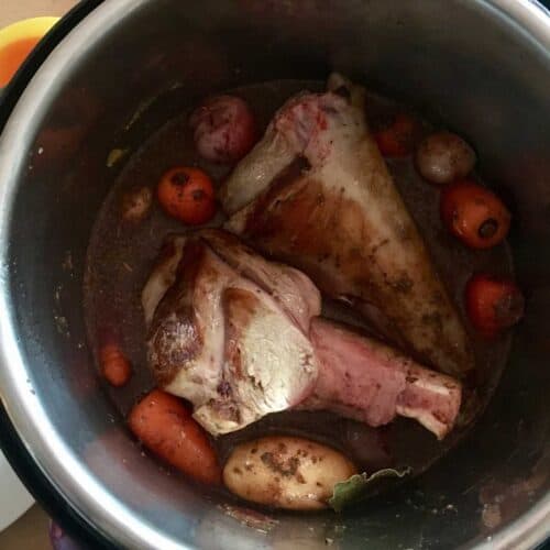 Lamb shanks seen from above inside the Instant Pot's stainless steel inner pot, with the potatoes and carrots showing underneath