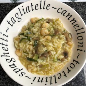 The pressure cooked risotto seen from above on a white plate that makes it look rather funny (the plate has the words spaghetti, tortellini, tagliatelle, cannelloni printed in black all around the rim)