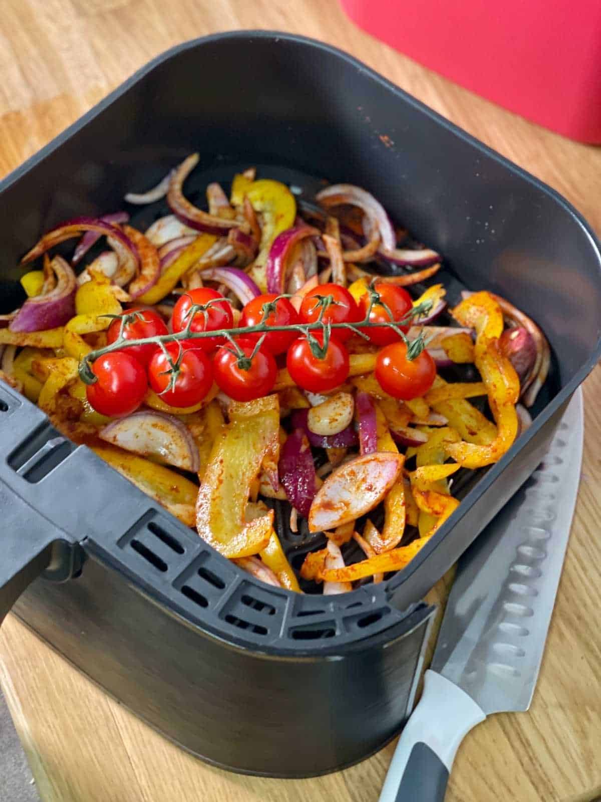 Sliced pepper, red onion, garlic mixed with paprika with cherry tomatoes on top, seen in Instant Vortex 4 in 1 drawer from above, there's a Zyliss Comfort Santoku knife on the side