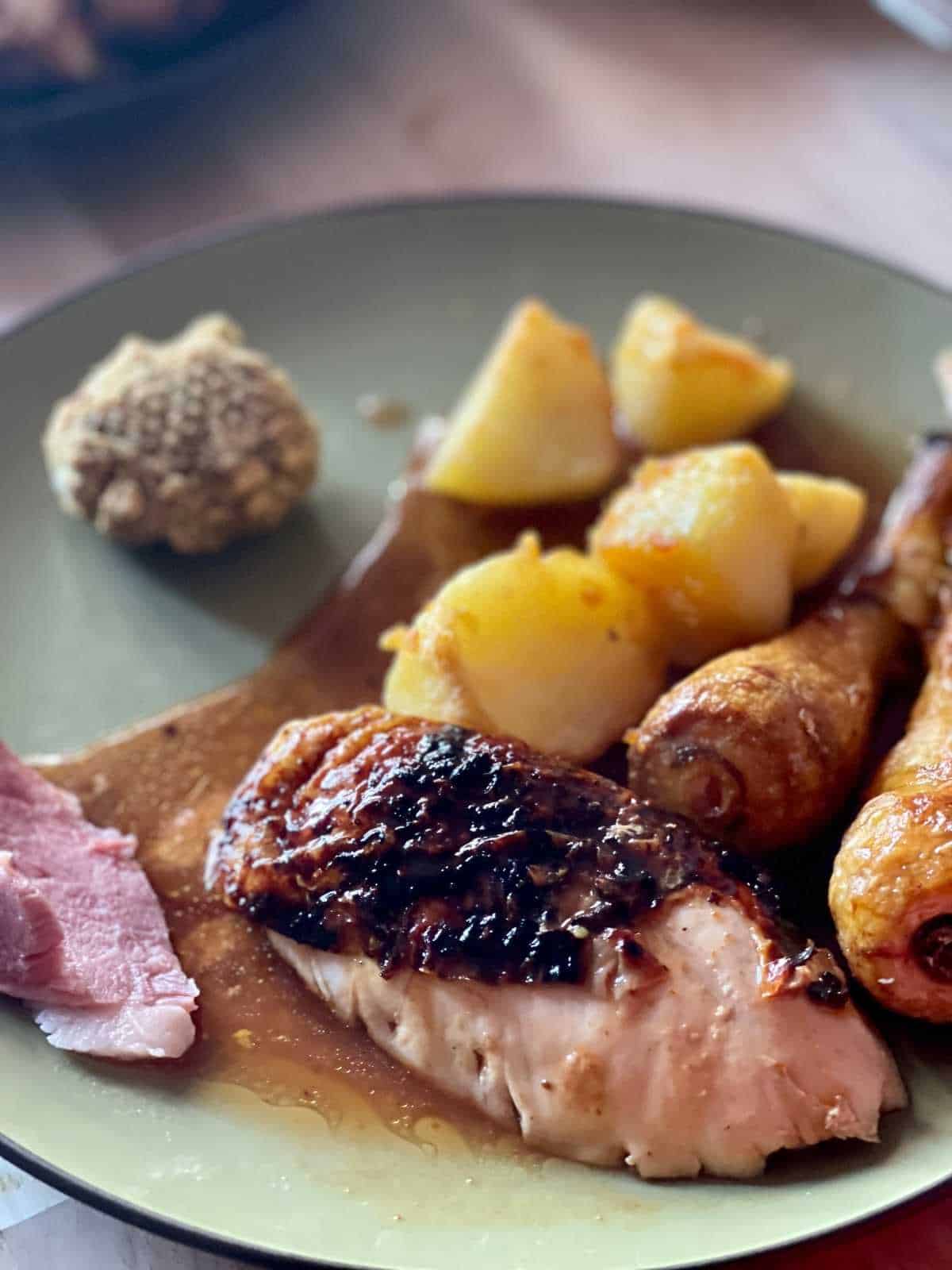 Chicken breast on a green dish with a dark brown or black rim, on the plate there's also the gravy from the air fryer, roast parsnips and potatoes, even a ball of stuffing