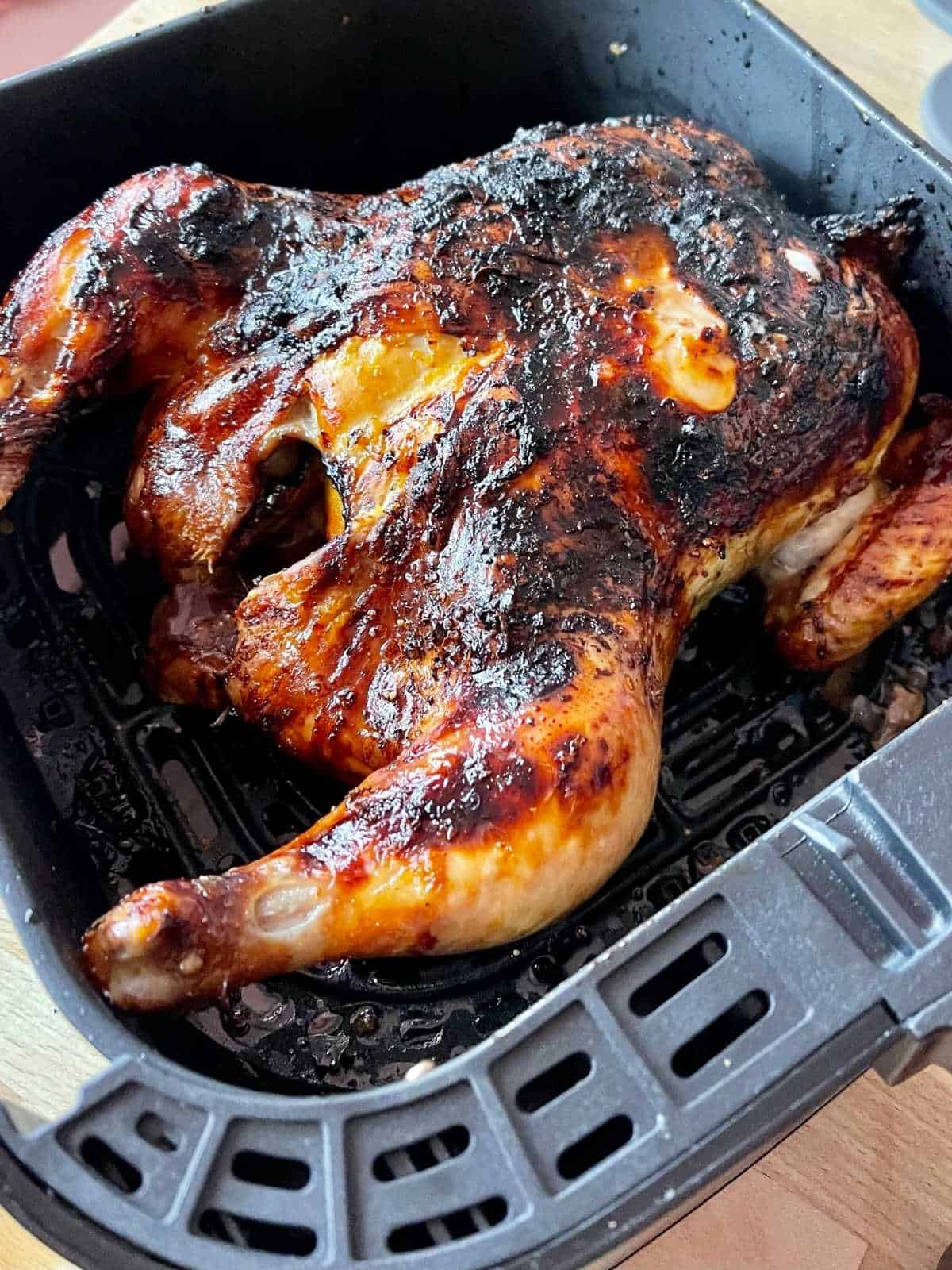 The finished air fryer whole roast chicken looking nice and juicy seen from above inside the Instant Vortex air fryer drawer, which has been placed on a light-coloured wooden surface