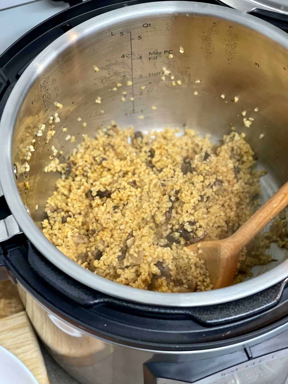Pressure cooked mushroom bulgur wheat seen from above in Instant Pot Duo Evo Plus - with a wooden spoon on the side