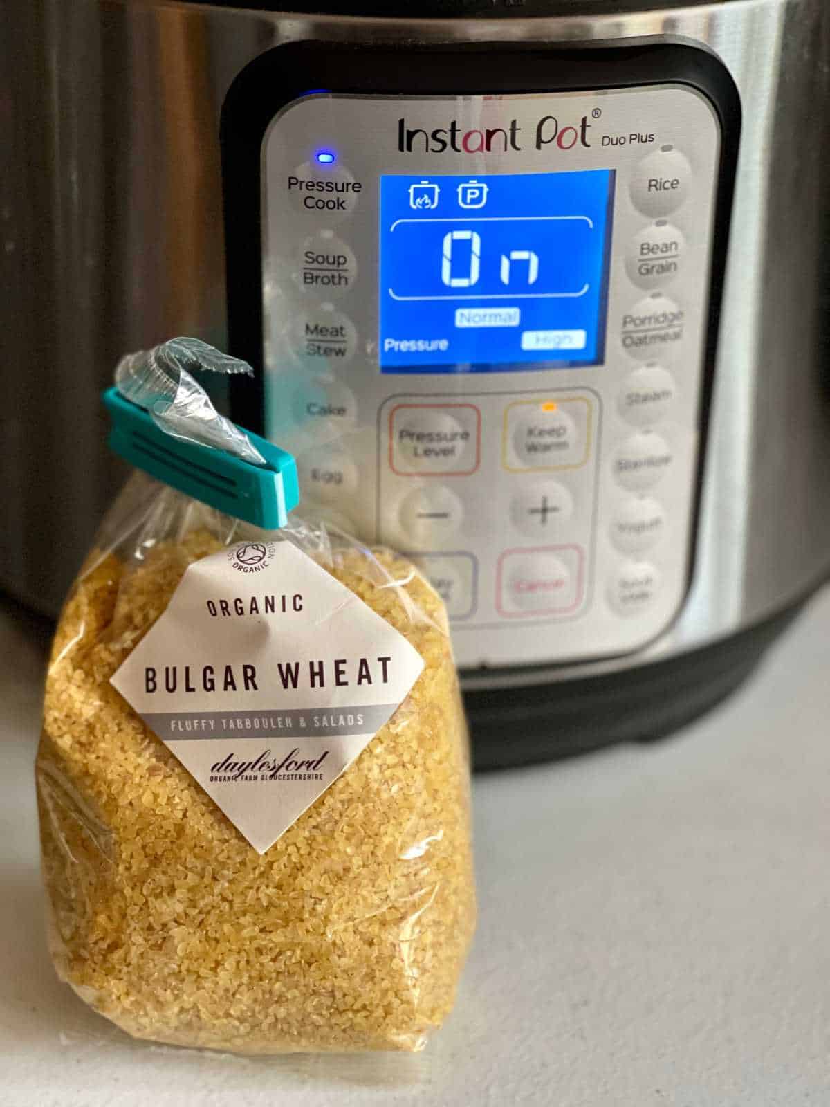 Bag of Daylesford Organic Bulgar Wheat standing up and being held together with a blue bag clip, seen with an instant pot duo plus in the background, on a white surface