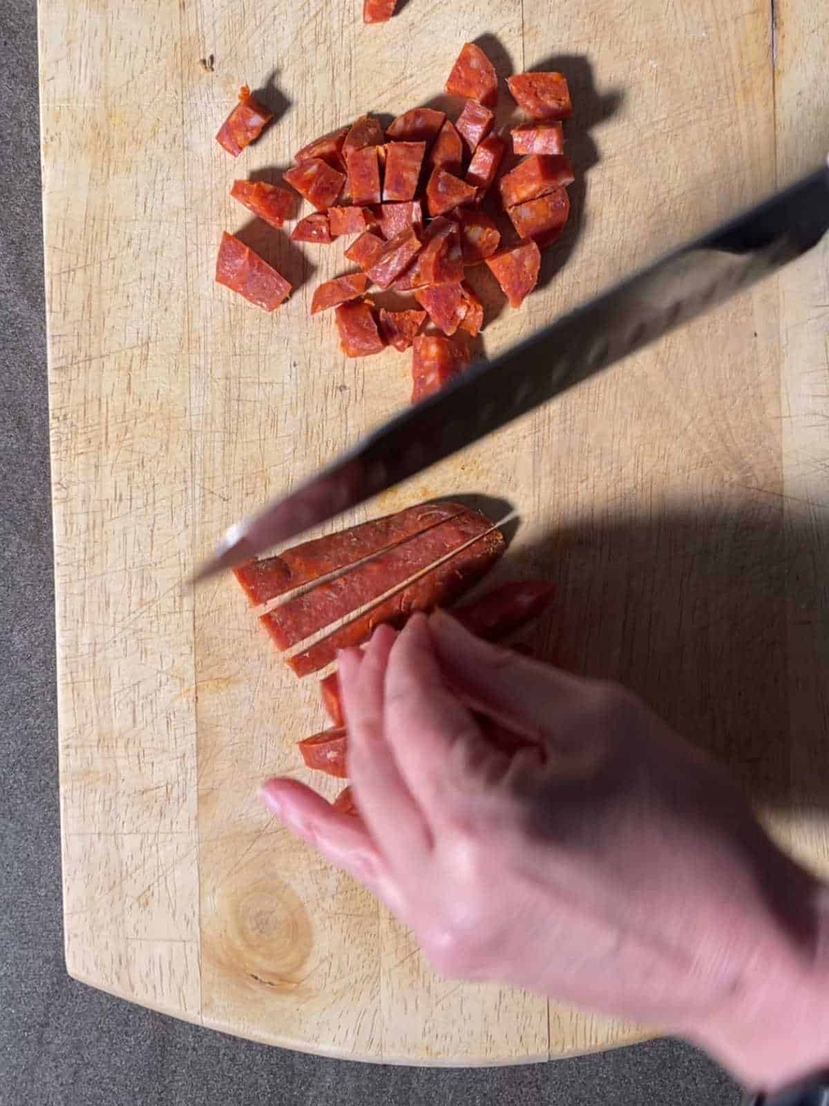 Overhead shot showing how to slice chorizo sausage lengthways and then dice it, this helps make the most of the juices it releases