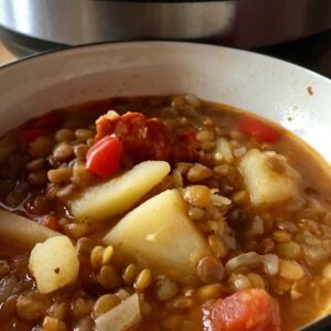 Pressure cooked Instant Pot Spanish Lentil Soup (Lentejas) seen in a beige bowl with an Instant Pot electric pressure cooker in the background