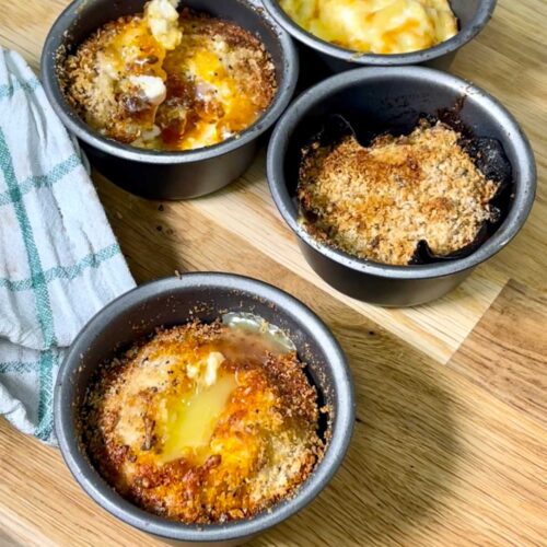 Air fried egg pots seen from above on a wooden chopping board with a white and green tea towel on the left